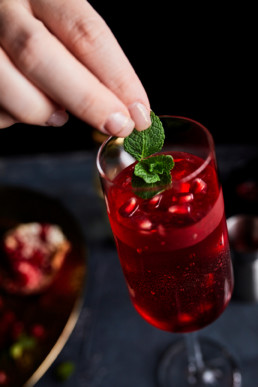 Adding fresh mint leaves as a garnish to pomegranate spritzer mocktail