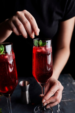 Adding fresh mint leaves as a garnish to pomegranate spritzer mocktail