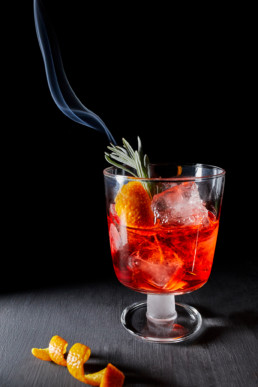 Negroni cocktail on ice with flamed rosemary and orange peel