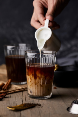 Pouring milk in a spiced black tea. Making chai latte.