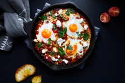 Shakshuka with tomatoes, peppers, onions and eggs prepared in cast iron skillet.