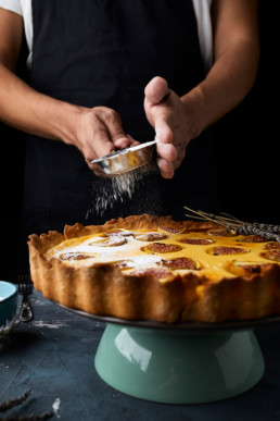 Sprinkling sugar powder on freshly baked mascarpone fig tart