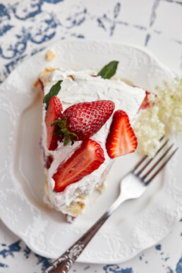 Peace of Pavlova cake with fresh strawberries garnished with mint leaves and elderflower